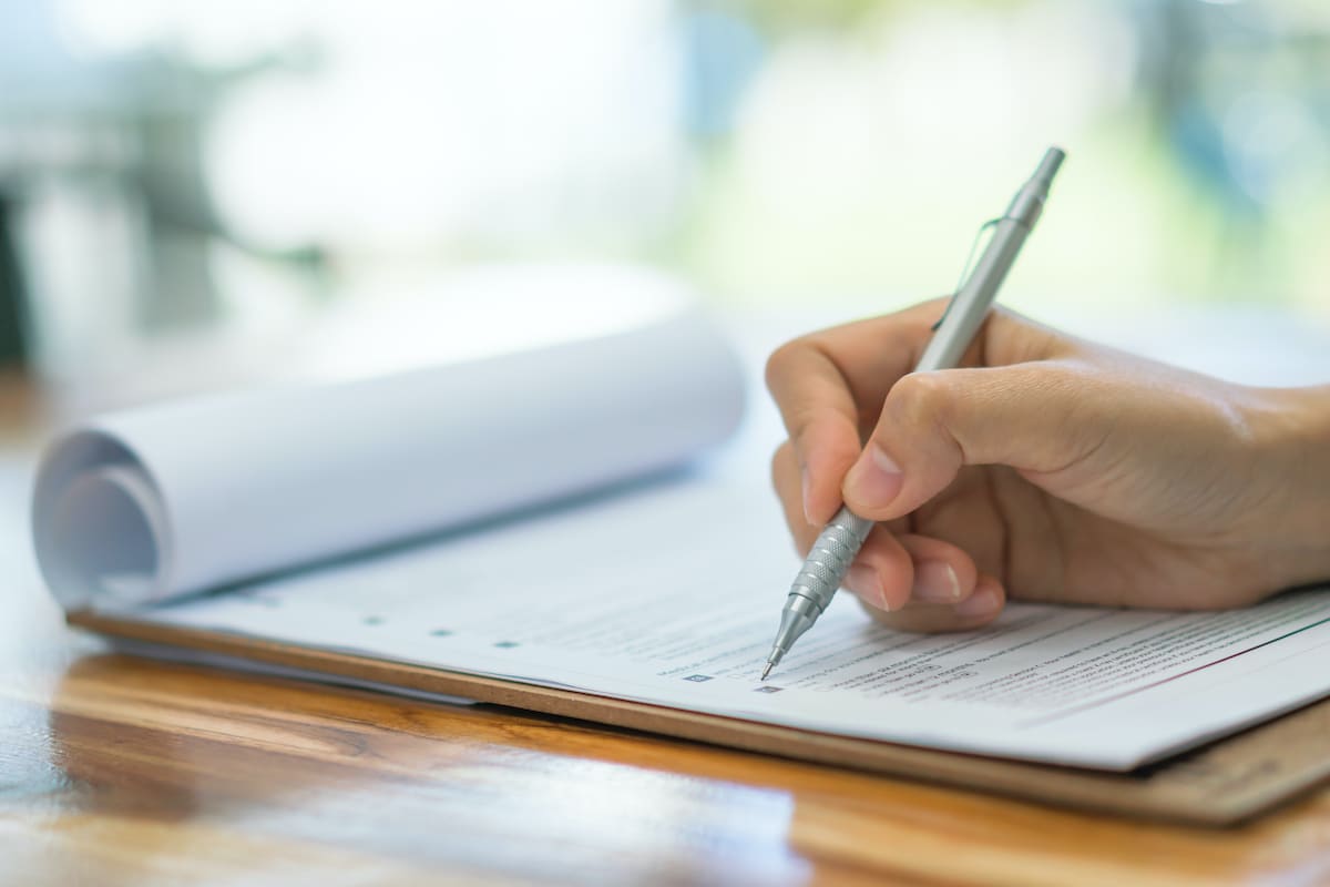 A hand filling out a survey on a clipboard.