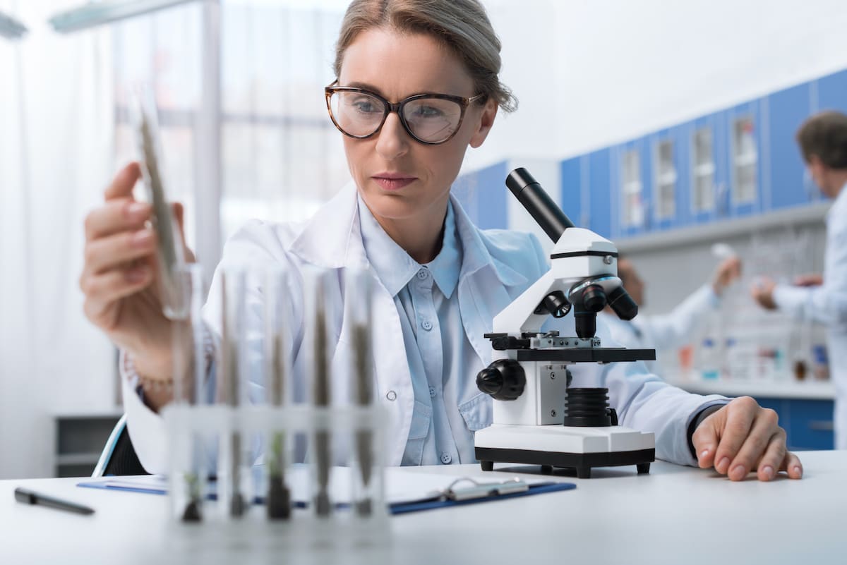 woman-researching-lab-coat-M A woman in a lab conducting research with vials.